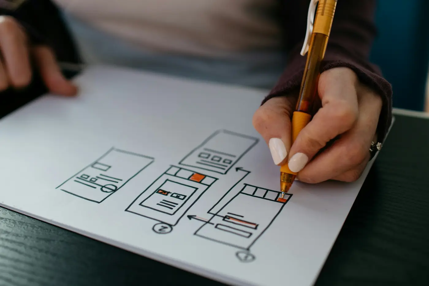 A hand sketching website wireframes on paper with an orange pen